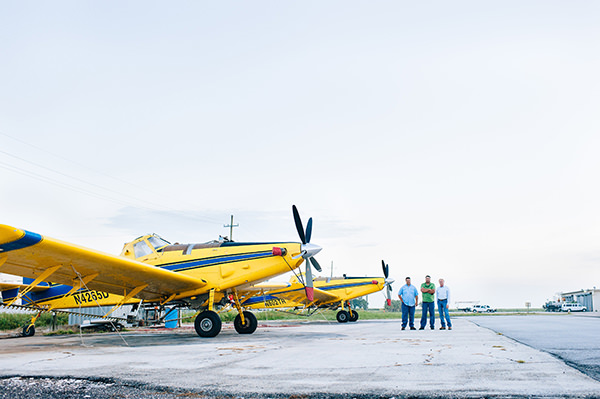 Three individuals stand beside two Air Tractor AT-502B agricultural aircraft on a runway, showcasing their commitment to aerial application. The planes are designed for efficiency in crop dusting and agricultural management.