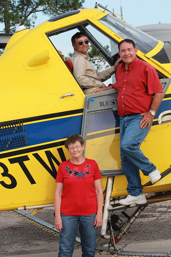 A group of three people stands near an Air Tractor AT-502B, a popular agricultural aircraft known for its efficiency in crop dusting and aerial application. The pilot is seated in the cockpit, while two individuals pose beside the plane, showcasing the aircraft's role in modern farming practices.