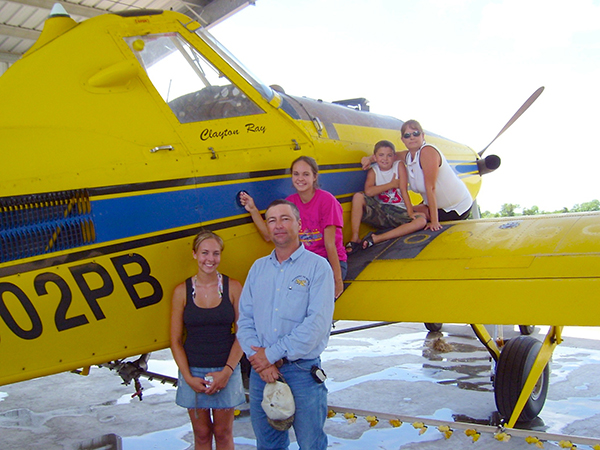 Air Tractor AT-502B aircraft with family members posing in front, showcasing agricultural aviation. The setting is a hangar, highlighting the plane's role in crop dusting and aerial application.