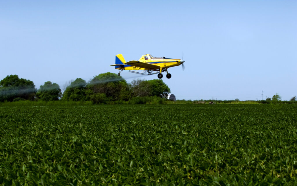 Air Tractor agricultural aircraft performing aerial application over a green field, showcasing efficient crop spraying capabilities.