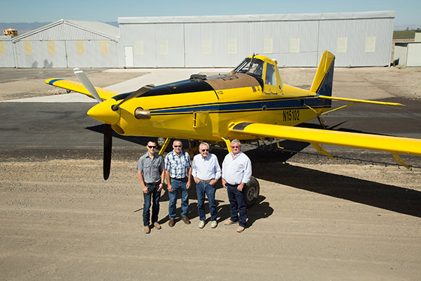 Four individuals standing in front of an Air Tractor AT-502B agricultural aircraft on a runway, showcasing the plane's robust design. The aircraft is equipped for aerial application and is part of Air Tractor's lineup of agricultural planes, known for their efficiency and durability.