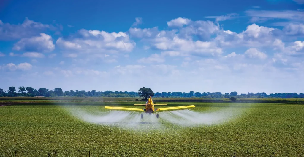 An Air Tractor aircraft flies toward the horizon spraying a green field below.