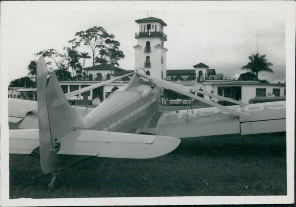 Air Tractor AT-502B airplane parked with a control tower and foliage in the background, showcasing its agricultural design.