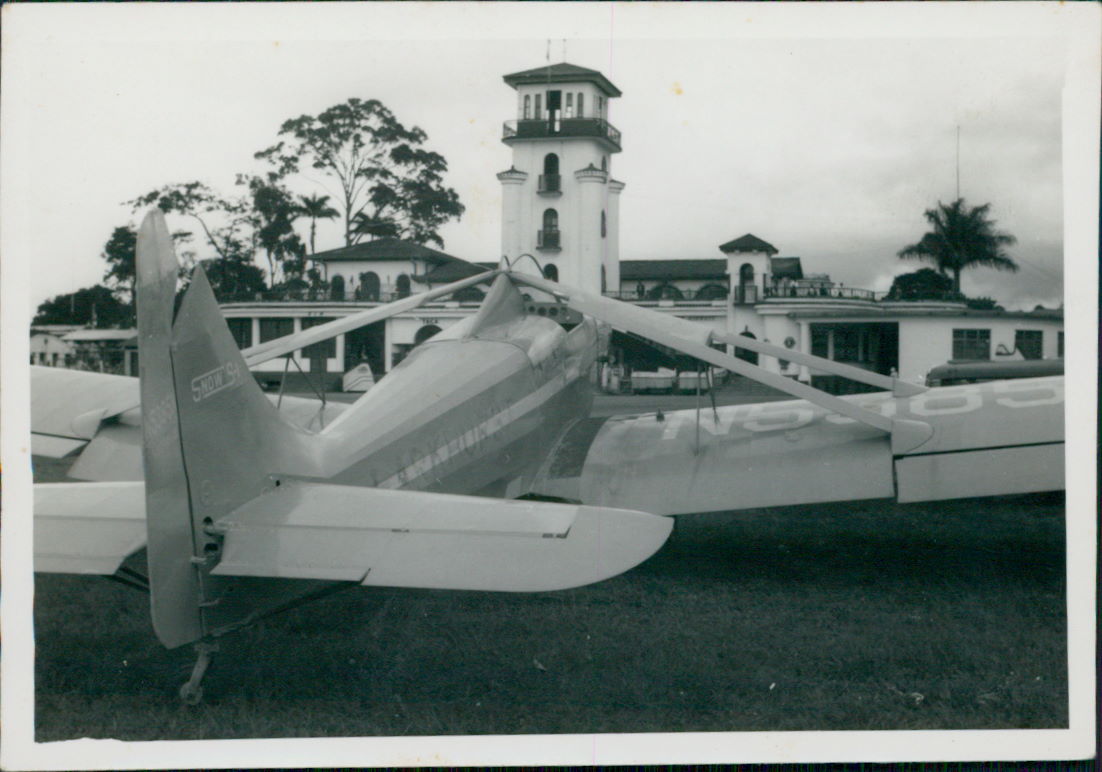 Air Tractor AT-502B airplane parked with a control tower and foliage in the background, showcasing its agricultural design.