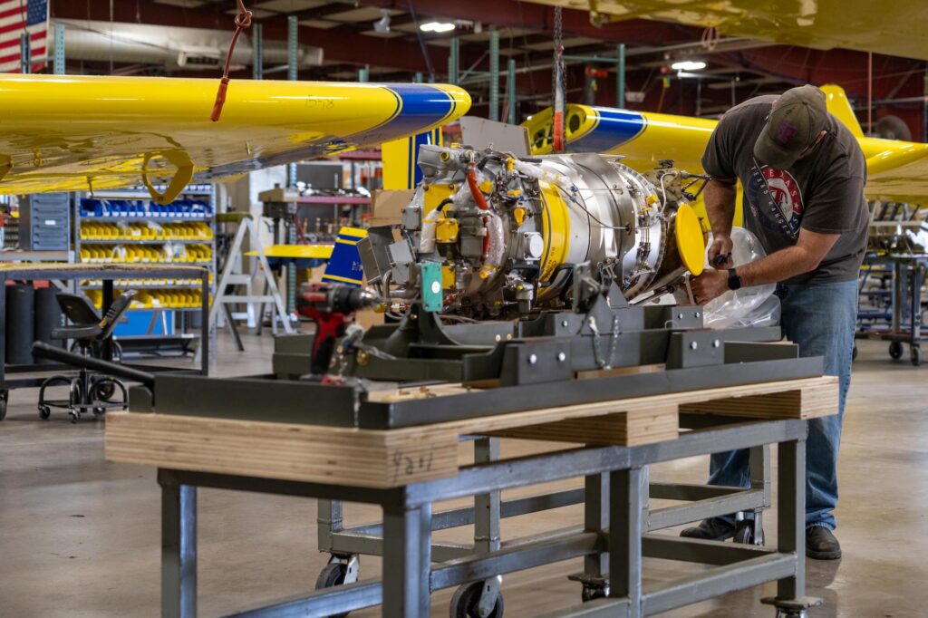 Mechanic working on the engine assembly of an Air Tractor aircraft in a manufacturing facility, showcasing the intricate components and assembly process of agricultural aviation technology.