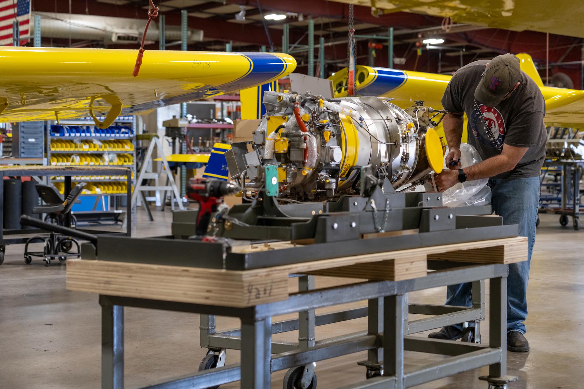 Mechanic working on the engine assembly of an Air Tractor aircraft in a manufacturing facility, showcasing the intricate components and assembly process of agricultural aviation technology.