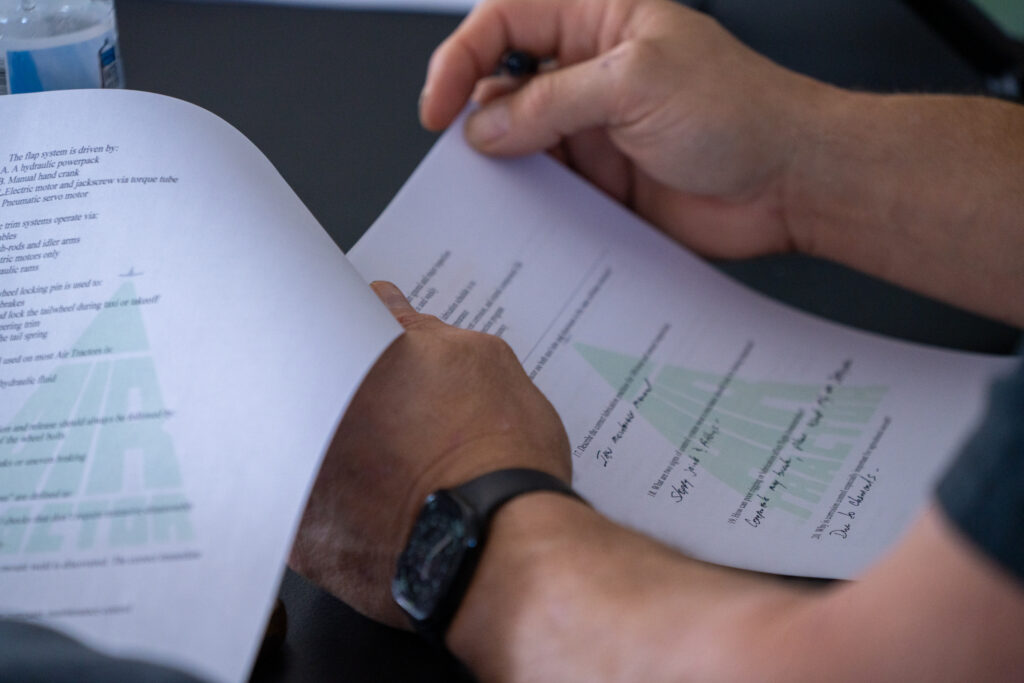 Hands holding a document with technical specifications related to the flap system of an Air Tractor aircraft, highlighting key components like hydraulic powerpack and trim systems.