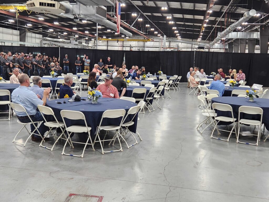 A gathering of attendees seated at tables in a large indoor space, likely an event related to Air Tractor, showcasing a community atmosphere. The background features staff and guests engaged in conversation, highlighting the company’s focus on collaboration and connection within the aviation industry.